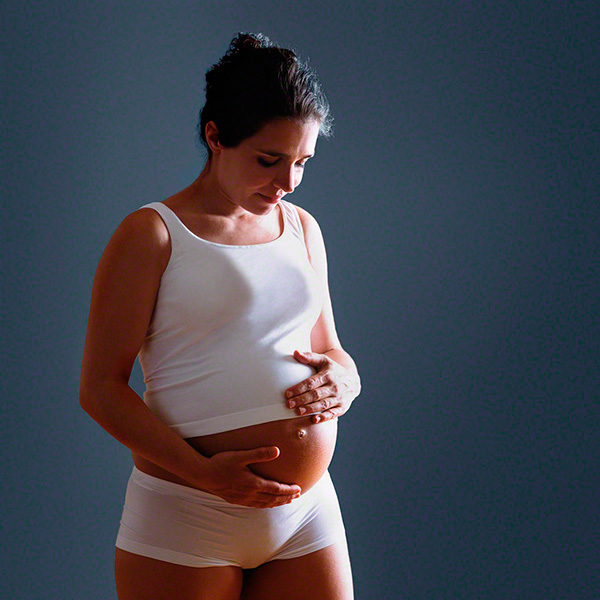 in studio portrait against dark background of pregnant woman staring at her belly