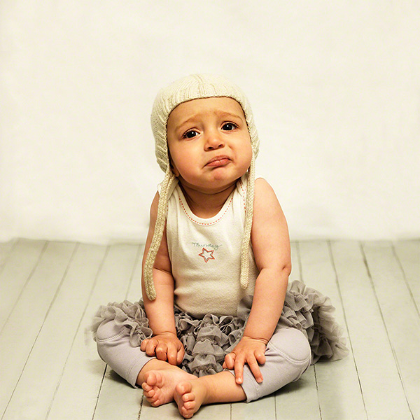 in studio against light background, cute portrait of little girl, 3 year-old on the verge of crying