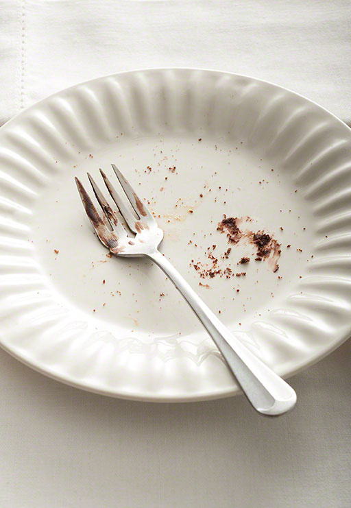 overhead shot of leftover dessert crumbs on a plate with fork, white on white texture background, editorial