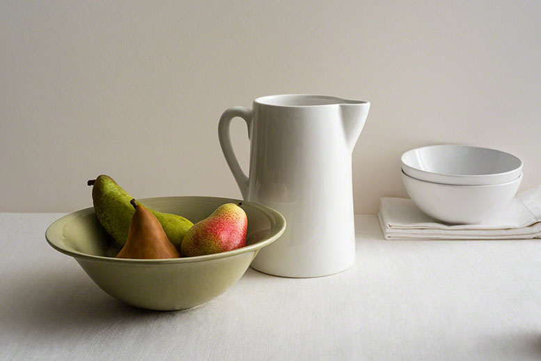 editorial muted table top shot of pears in a bowl with white ceramic pitcher, classic, three quarter shot, stillife