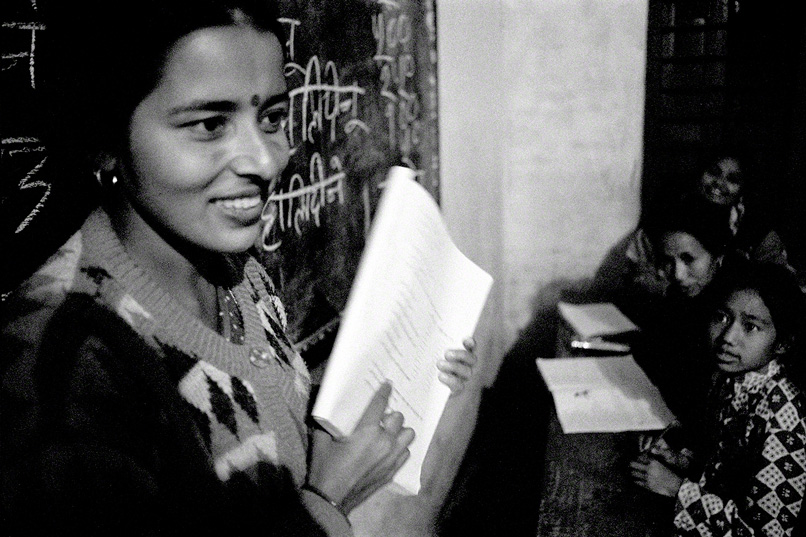 female teacher holds up workbook at the front of the class while students look on