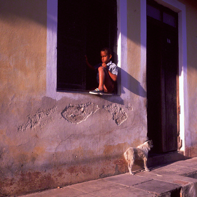 young boy sitting on window sill in the shadows of the mid-day sun