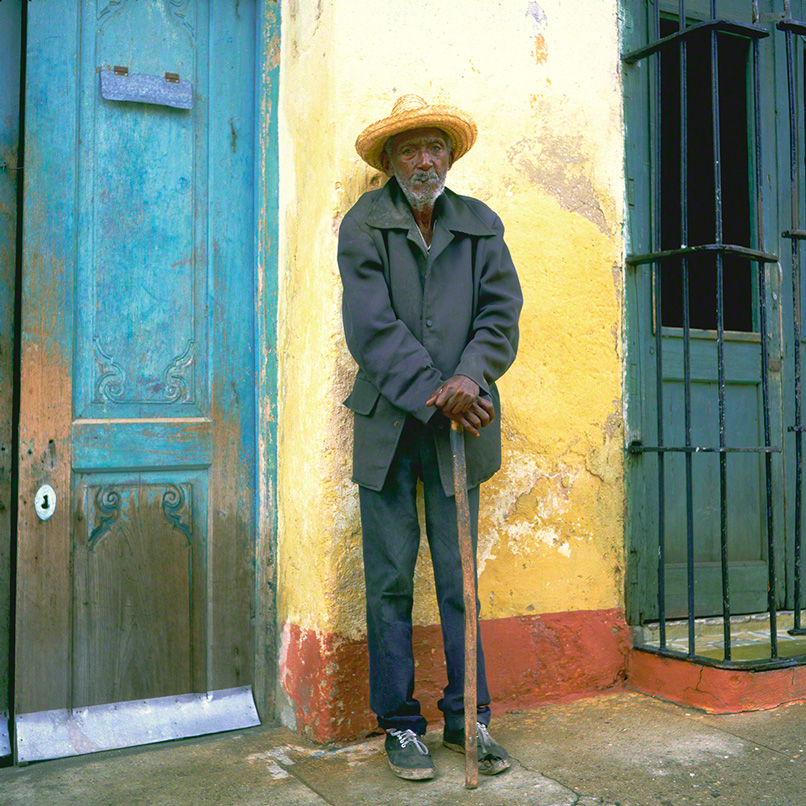 portrait of an old man leaning against a yellow wall